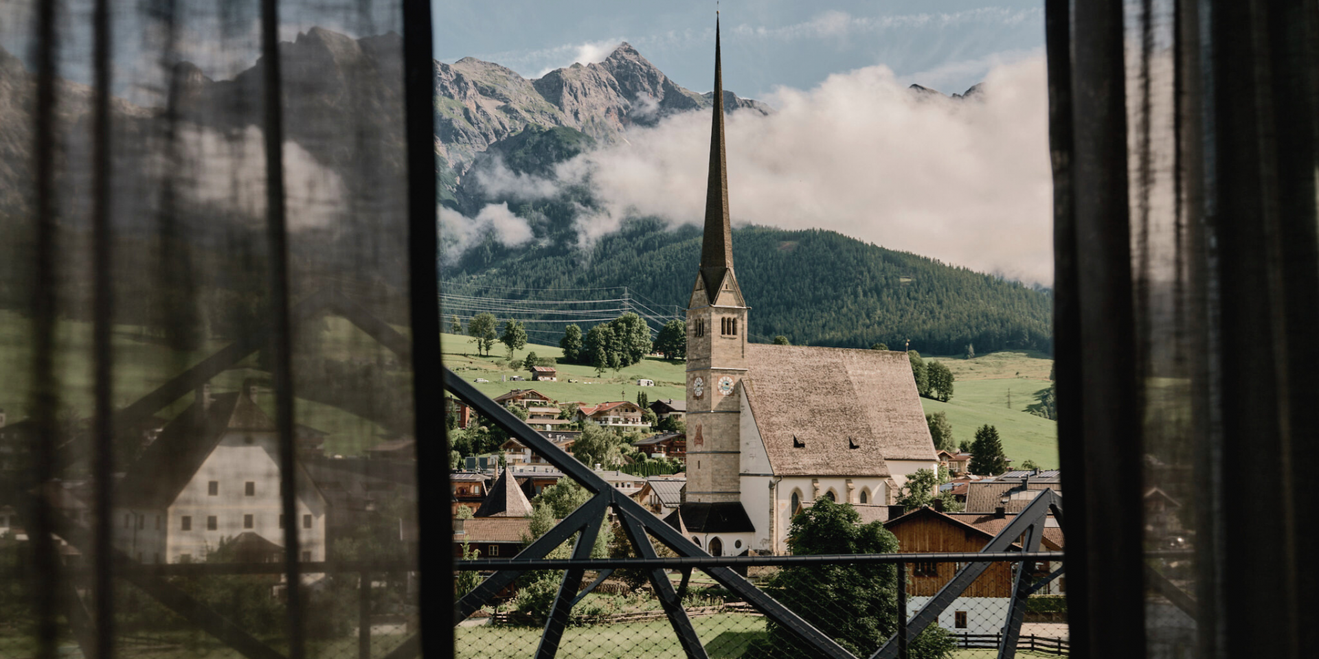 View of the mountains and the village church with a slightly transparent curtain in the foreground