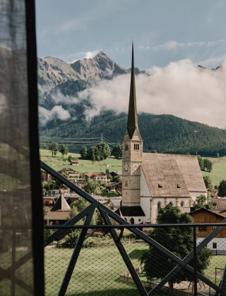 Ausblick auf die Berge und die Dorfkirche mir leicht durchsichtigem Vorhang im Vordergrund