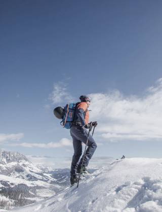 Skitourengeher im Schnee mit blauem Himmel, Sonnenschein und Berge im Hintergrund