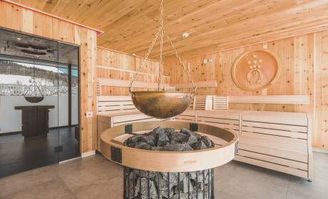 Fireplace standing in the middle of a sauna made of wood, with coal and an iron bowl above it