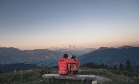 Paar sitzt am Gipfel auf einer Bank und hat eine fantastische Aussicht auf die Berge und die Landschaft