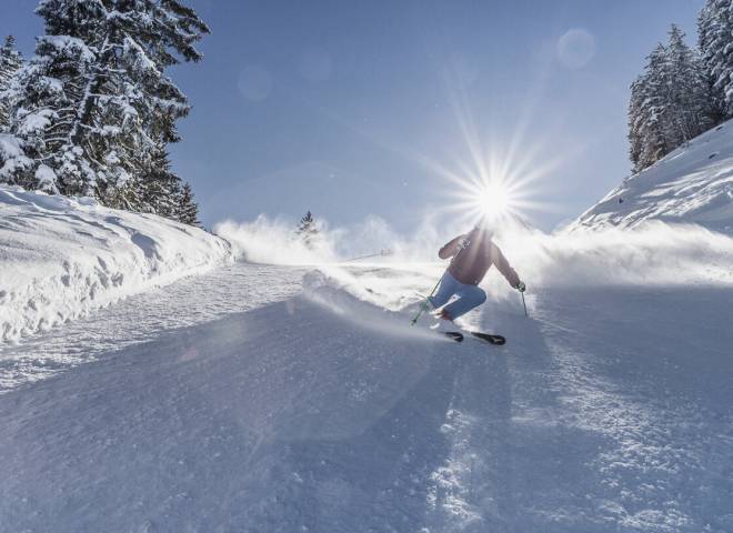 Skiers skiing down a piste with blue sky and sunshine