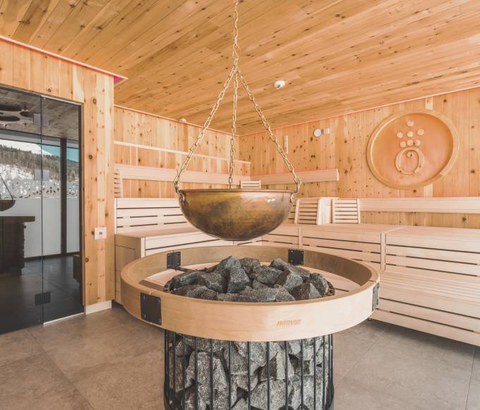 Fireplace standing in the middle of a sauna made of wood, with coal and an iron bowl above it